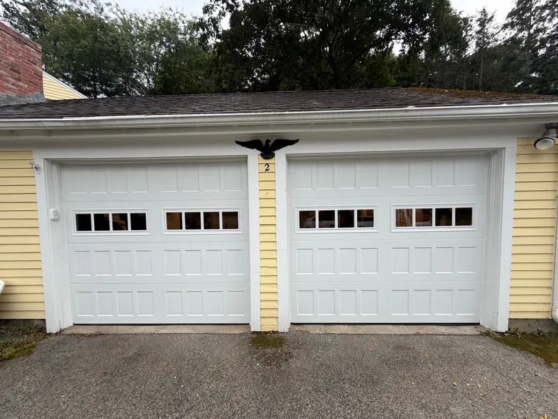 Two new white Amarr Hillcrest garage doors with a row of windows on a yellow house in Acton, MA
