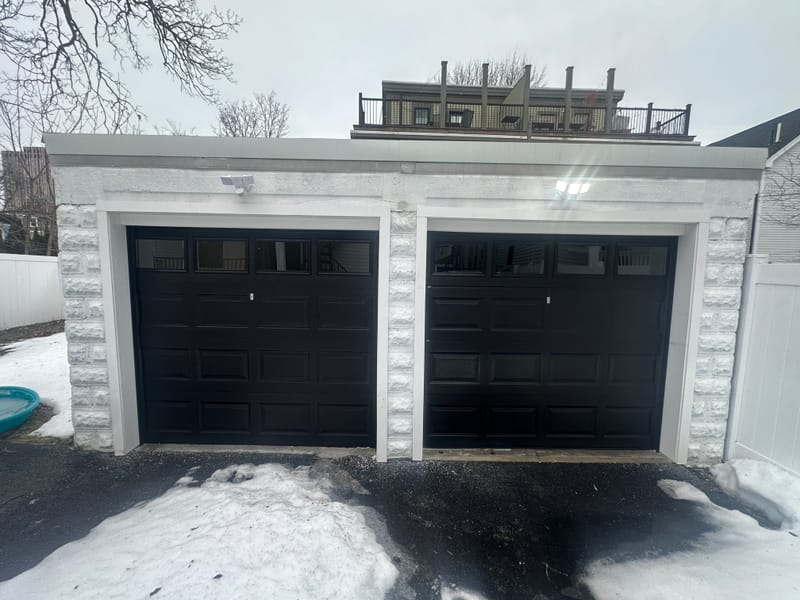 Two black garage doors with windows on a white block garage in winter