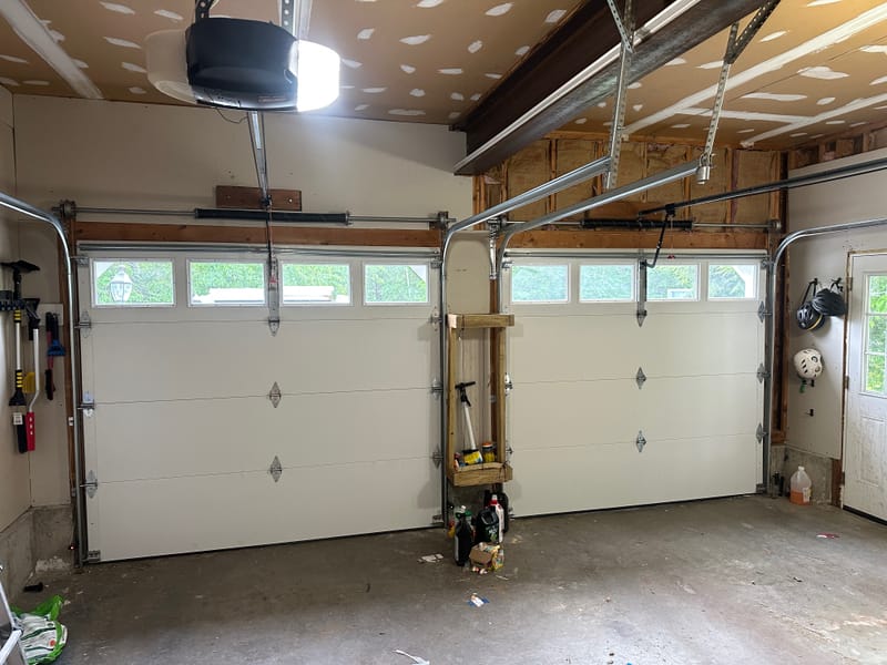 Inside a two-car garage after the install: two new white doors with windows and a torsion spring above each door
