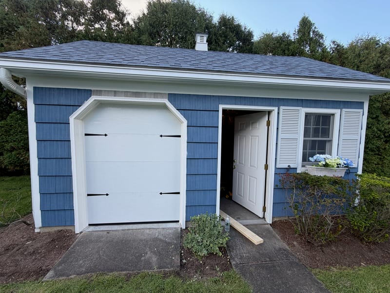 Narrow white flush-panel garage door with black strap hinges on a blue garage in Chelmsford, MA