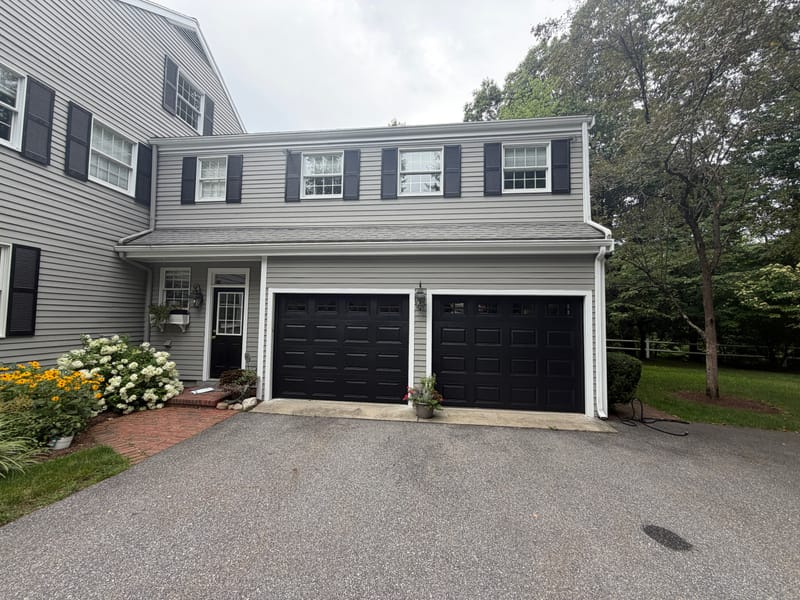 Two black raised-panel garage doors with windows on a gray colonial