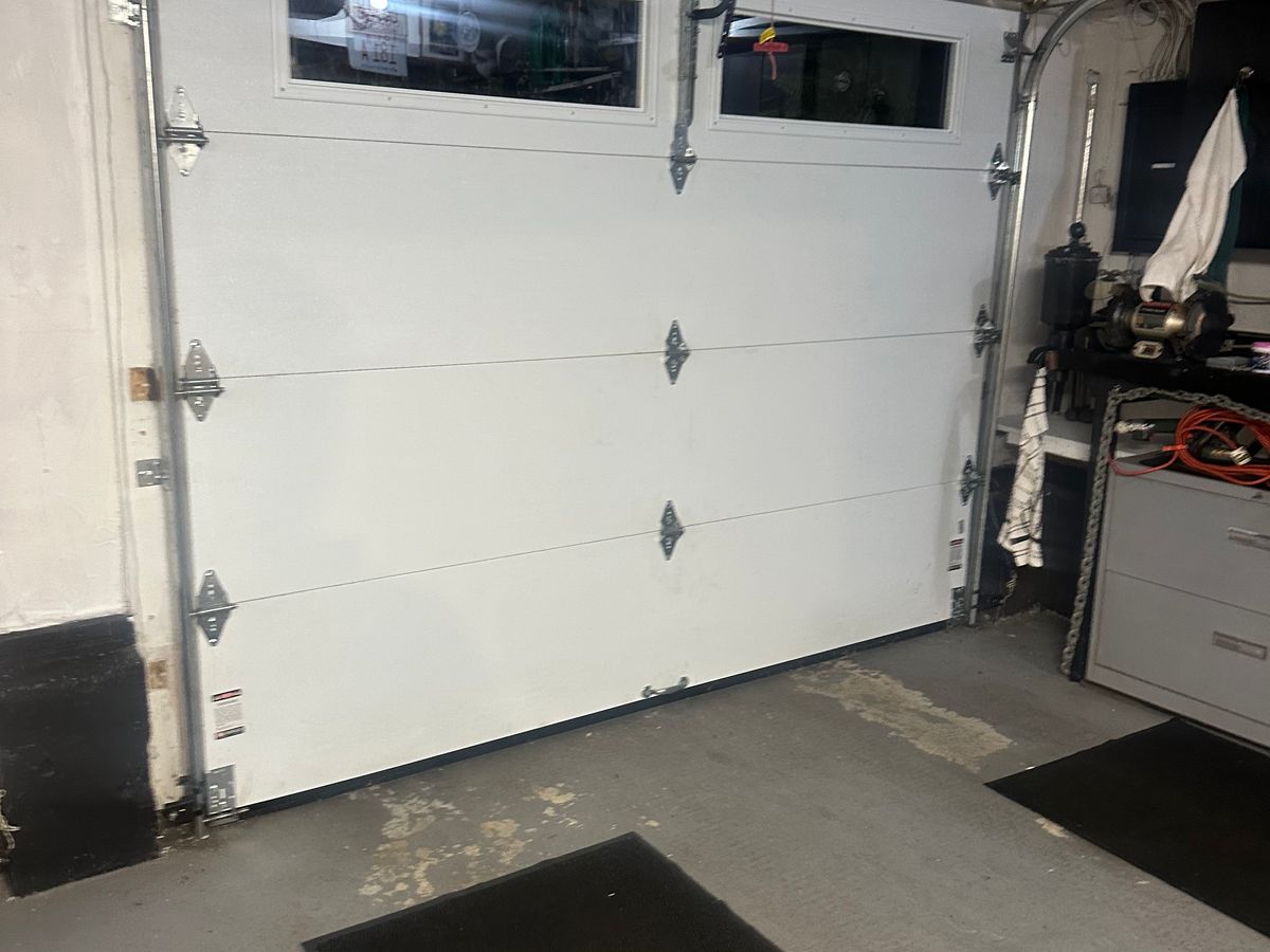 Inside view of a white commercial sectional door with windows, the hoist hand chain hanging beside the track