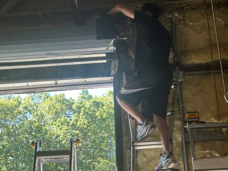 Technician on a ladder working at the top of an open commercial overhead door