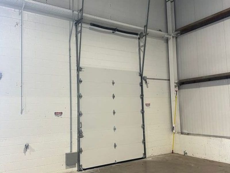 Large white commercial sectional door seen from inside, closed, with its tracks running up the wall