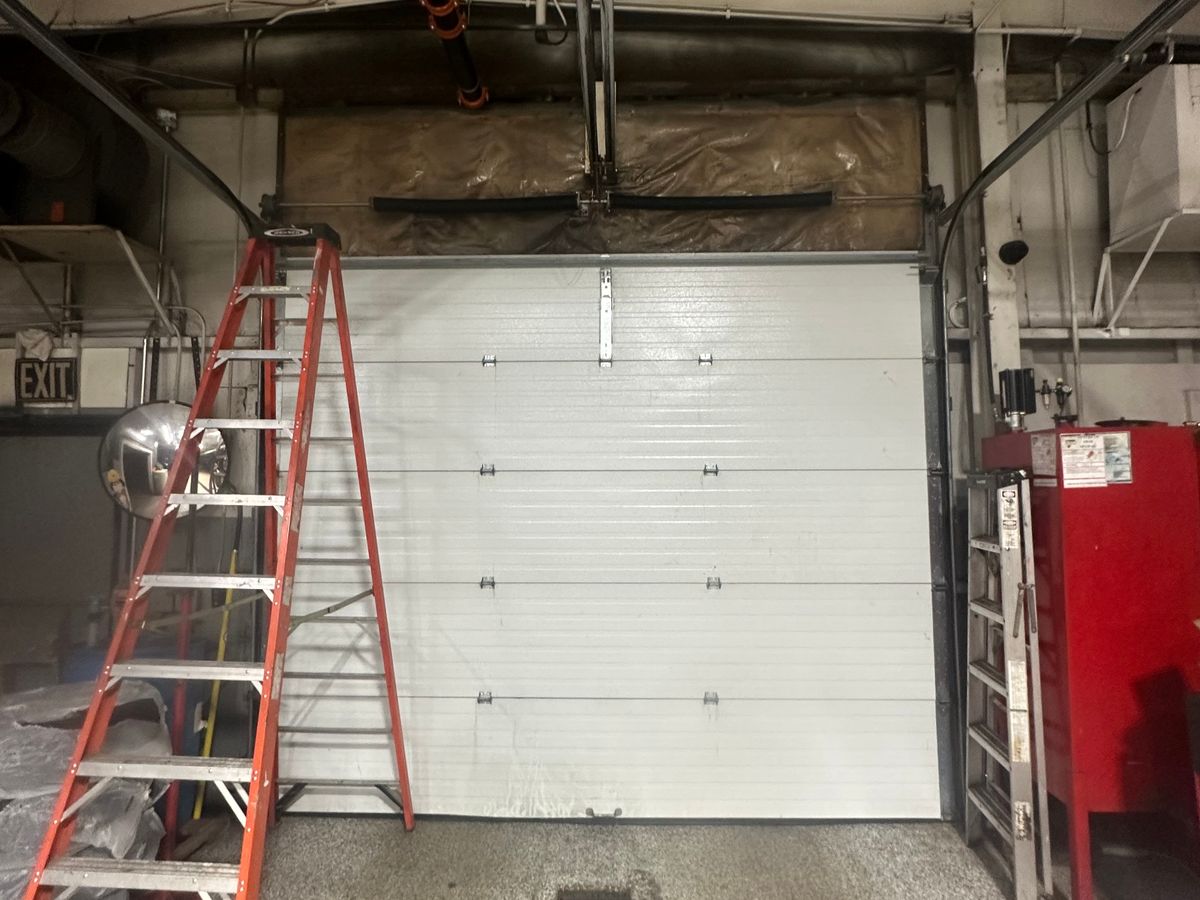 Commercial insulated sectional door interior with LiftMaster opener and ladder during service