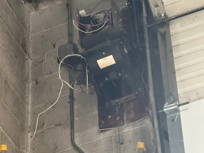 Old wall-mounted commercial door opener on a block wall, its wiring exposed during repair