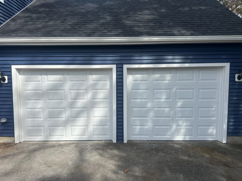 Two new white raised-panel garage doors on a navy two-car garage, replacing worn doors