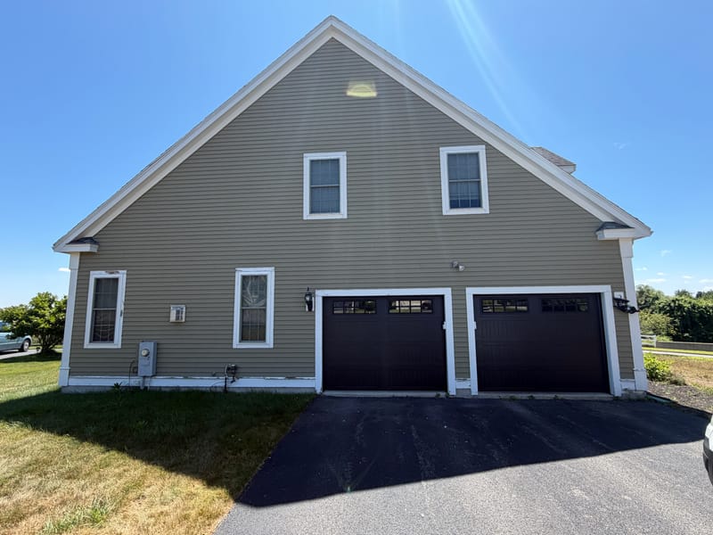 Gable end of a tan house in North Andover, MA with two new black long-panel garage doors