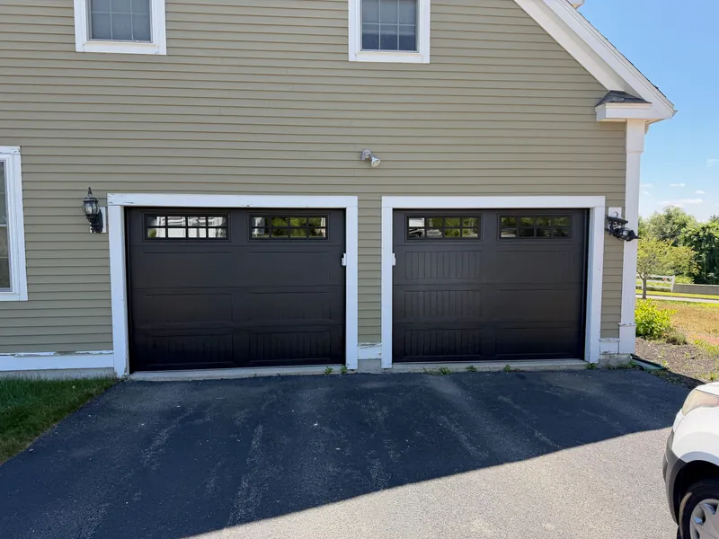 Two new black long-panel garage doors with Stockton windows on a tan house in North Andover, MA